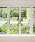 View through sliding glass doors to a garden with pool, trees, and plants, showcasing outdoor scenery.