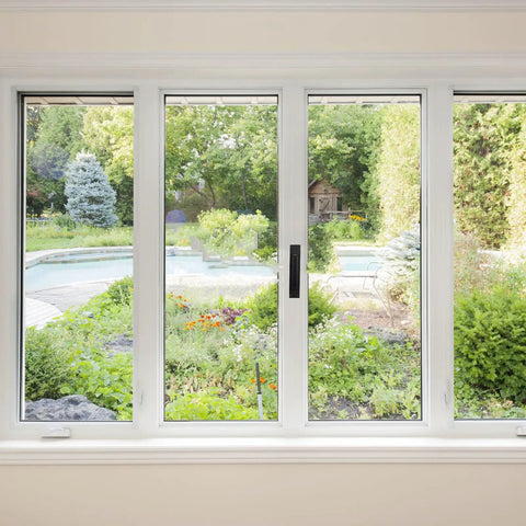 View through sliding glass doors to a garden with pool, trees, and plants, showcasing outdoor scenery.