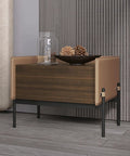 Modern square table with brown wood body and leather accents, featuring decorative bowl and glass jar on top.