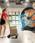 Real Deal High Capacity Industrial Warehouse Floor Fan Featuring Slick Aerodynamic Blades For Far Reaching Cool Breeze Built Tough Anti Tip Base And Smooth Casters with worker and cart in warehouse.