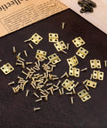 Set Of One Hundred Gold Mini Brass Hinges For Small Boxes And Crafts Featuring Easy Peasy Assembly with tiny screws on a dark background.