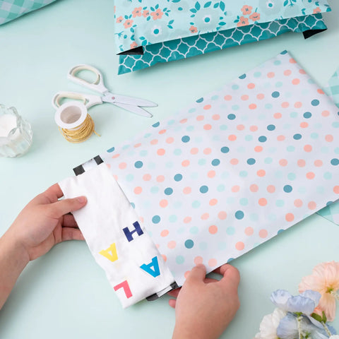 Hands placing items in thick self adhesive poly mailers 10x13 inches 40 pack durable padded envelopes with spring dot plaid flower design