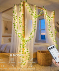 Vine With Fairy Lights Battery Operated 33Ft 100 LED Pothos String Lights With Remote Warm White Leaves on a bed canopy.