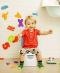 A joyful toddler sitting on The Real Deal Toddler Potty Training Chair 3-In-1 Potty Seat with colorful letters flying around.