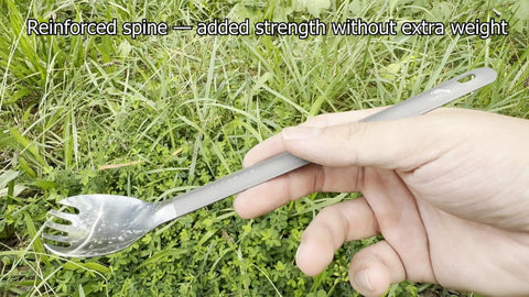 Hand holding Ultra Lightweight Titanium Long Handle Spork With Polished Bowl For Camping And Hiking over grass