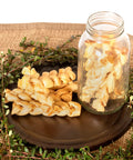 American Beefhide 6-Inch Braided Dog Chew Stix With Chicken Flavor on a dark round plate next to a jar filled with chews.