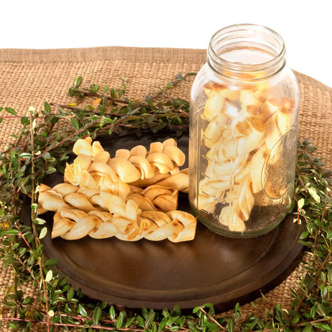 American Beefhide 6-Inch Braided Dog Chew Stix With Chicken Flavor on a dark round plate next to a jar filled with chews.