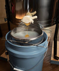 Honey flowing into a bucket through a stainless steel honey strainer with dual sieve for beekeeping fine and coarse mesh filter.