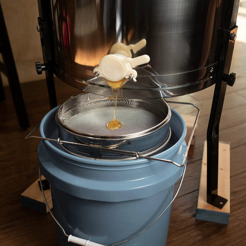 Honey flowing into a bucket through a stainless steel honey strainer with dual sieve for beekeeping fine and coarse mesh filter.