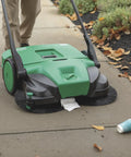 Deluxe Triple Brush Push Power Sweeper Boasts 38 Inch Wide Cleaning Deck And Huge 13 2 Gallon Hopper cleaning leaves and trash on sidewalk.