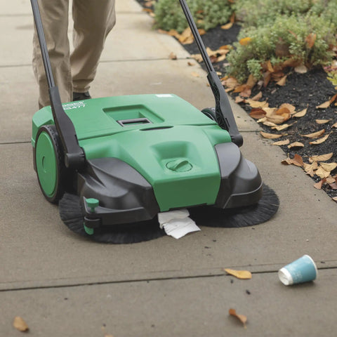 Deluxe Triple Brush Push Power Sweeper Boasts 38 Inch Wide Cleaning Deck And Huge 13 2 Gallon Hopper cleaning leaves and trash on sidewalk.