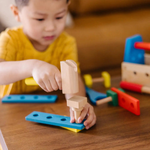 Child playing with Take Along Tool Kit Wooden Construction Toy Set for Little Builders with 24 pieces including hammer and boards