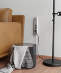 Slick Black Smart Power Strip With WiFi App Control, Heavy Duty Surge Protector, Built In USB Charging Ports beside a cozy sofa.