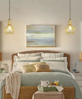 Bedroom with two hanging lamps, wicker bed, artwork, and bedside tables.