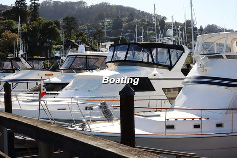 Boats docked in a marina with trees and hills in the background, featuring white and blue watercraft with cabin enclosures.