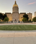Front view of a historic building with a dome, surrounded by trees and a green lawn at sunset.