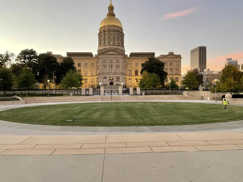 Front view of a historic building with a dome, surrounded by trees and a green lawn at sunset.