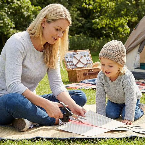 Professional laser-guided fabric scissors with ergonomic handle cutting fabric outdoors on a picnic mat.