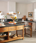 Rustic kitchen with wooden cabinets and black countertops, featuring a bright, sunlit atmosphere and a minimalist design.