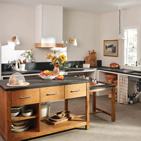 Rustic kitchen with wooden cabinets and black countertops, featuring a bright, sunlit atmosphere and a minimalist design.