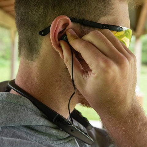 Man adjusting Behind The Neck Bluetooth Hearing Enhancer For Hunters With Retractable Earbuds, worn around neck