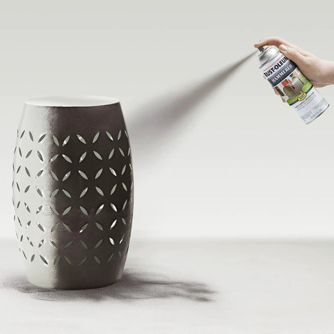 Hand spraying Badass Hammered Spray Paint In Sleek Dark Bronze on decorative metal vase with intricate cutouts.