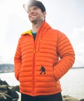 Person wearing an orange puffer jacket outdoors near a body of water with a Bigfoot silhouette on the pocket.