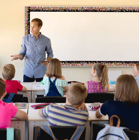 Teacher in classroom with students, Colorful Confetti On Black Border Trim Roll 50 Foot To Liven Up Classroom Decor visible on board.