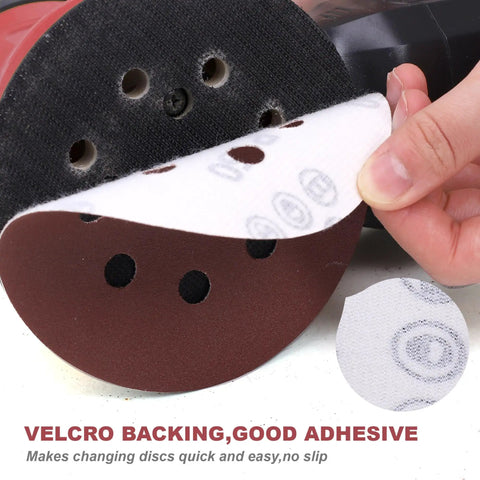 Peeling 5-inch sanding disc with velcro backing, showing 8-hole design. 200-Piece 5-Inch Sanding Discs Set With 8-Hole Hook And Loop Orbital Sandpaper Assorted Grit Pack Includes 40 60 80 100 120 150 180 240 320 400 600 800 1000 Grits For Woodwork And Metal Finishing Great For DIYers