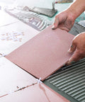 Pink ceramic tile being installed with white cross spacers on a mortar bed; 1/16 inch tile levelers.