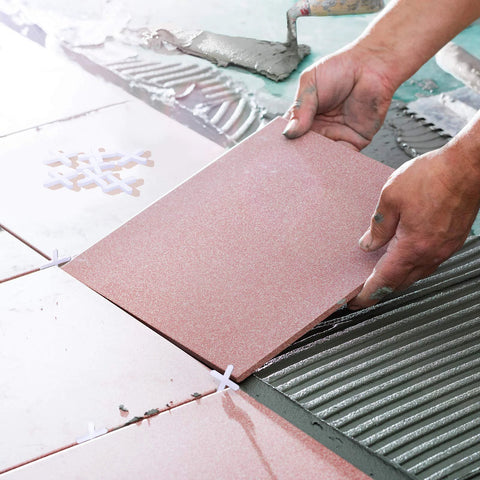 Pink ceramic tile being installed with white cross spacers on a mortar bed; 1/16 inch tile levelers.