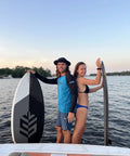 Two people on a boat holding Mondo 5 Foot 2 Inch Wakesurf Board with EVA Padding and Thruster Fin Design at a lake.