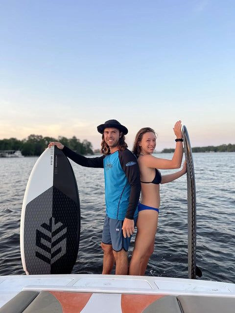 Two people on a boat holding Mondo 5 Foot 2 Inch Wakesurf Board with EVA Padding and Thruster Fin Design at a lake.