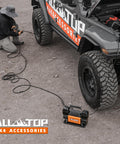 Heavy Duty 12V Dual Cylinder Portable Air Compressor Kit inflating off-road truck tire at outdoor location