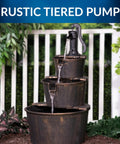 40 Inch Rustic Tiered Barrel Water Fountain For Outdoors with three stacked barrels next to a fence, in a garden setting.