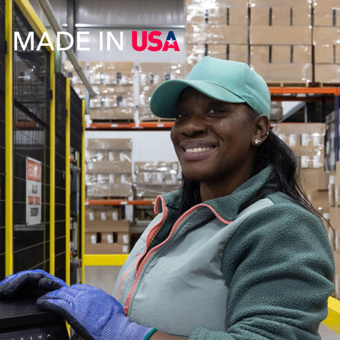 Smiling factory worker in teal cap and gloves at production line, with Made in USA text and stacked boxes in background.