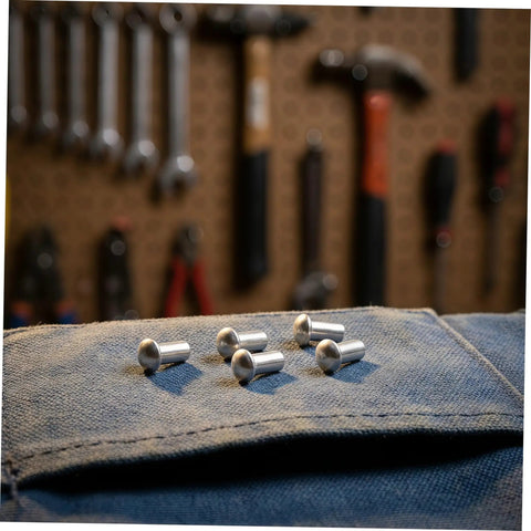 Five Two Hundred Aluminum Brazier Head Rivets M5x10 Millimeters With A Sleek Silver Dome Shape on denim fabric.