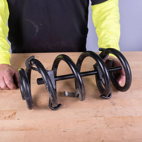 Person holding heavy-duty coil spring compressor tool for cars and trucks with built-in locking detent latches.