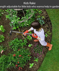 Child using kids rake in garden with adjustable handle, surrounded by vibrant green plants and flowers.