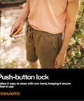 Person holding Foldable Produce Knife For Garden Harvests with one-handed safety lock in a garden setting.