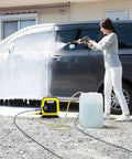Woman using water suction hose with filter for electric pressure washers to clean car, hose connected to pump and water tank