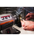 Shop Ready Six Inch Bench Grinder Powered By A Half Horsepower Motor Spinning 3450 RPM with hands working on metal piece.