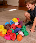 Child smiling at colorful pieces in 32 Piece Rock Climbing Holds Set For Kids And Adults on carpeted indoor floor.
