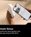 Person setting up a Smart Carbon Monoxide Detector And Indoor Air Quality Monitor With Real Time Alerts No Subscription Needed Plug In With Battery Backup 2 4 GHz Wi Fi Rotating Plug 85 dB Alarm IAQ Insights For Homes using a smartphone with the Kidde app on a wooden table.