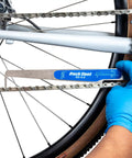 Mechanic using No Guesswork Bicycle Chain Wear Checker Pro Grade Gauge on bike chain with blue gloves.