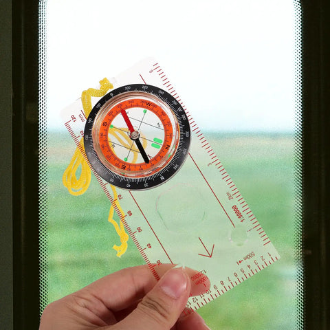 Handy Outdoor Hiking Compass With Map Scale Multifunction Navigation Tool held up close by a window.