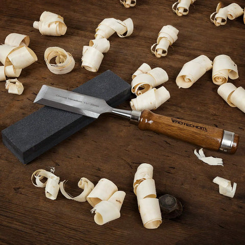 Pro-Grade 10-Piece Woodworking Chisel Set With Wooden Box, Honing Guide, Sharpening Stone, Razor-Sharp CR-V Steel Blades, Teak Handles, Rockwell C60 Hardness For Ultra Precise Carving And Smooth Finishes. Teak handle chisel with sharpening stone and wood shavings.