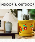 Indoor and outdoor decor featuring a gray lamp on a table and a yellow flower-painted pot with a succulent.