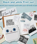 Pocket Sized Portable Bluetooth Mini Sticker Maker With Slick Inkless Thermal Tech And One Roll Of Glossy Paper For Snappy Journaling on a flat lay with various printouts.