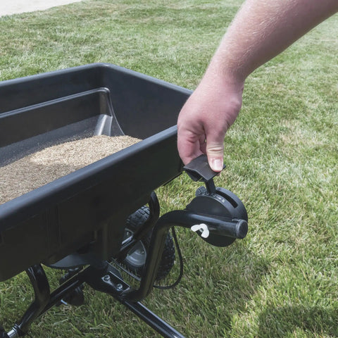 Tow Behind Broadcast Spreader With 85 Lb Capacity For Lawns, hand adjusting tractor seat on/off control near grass